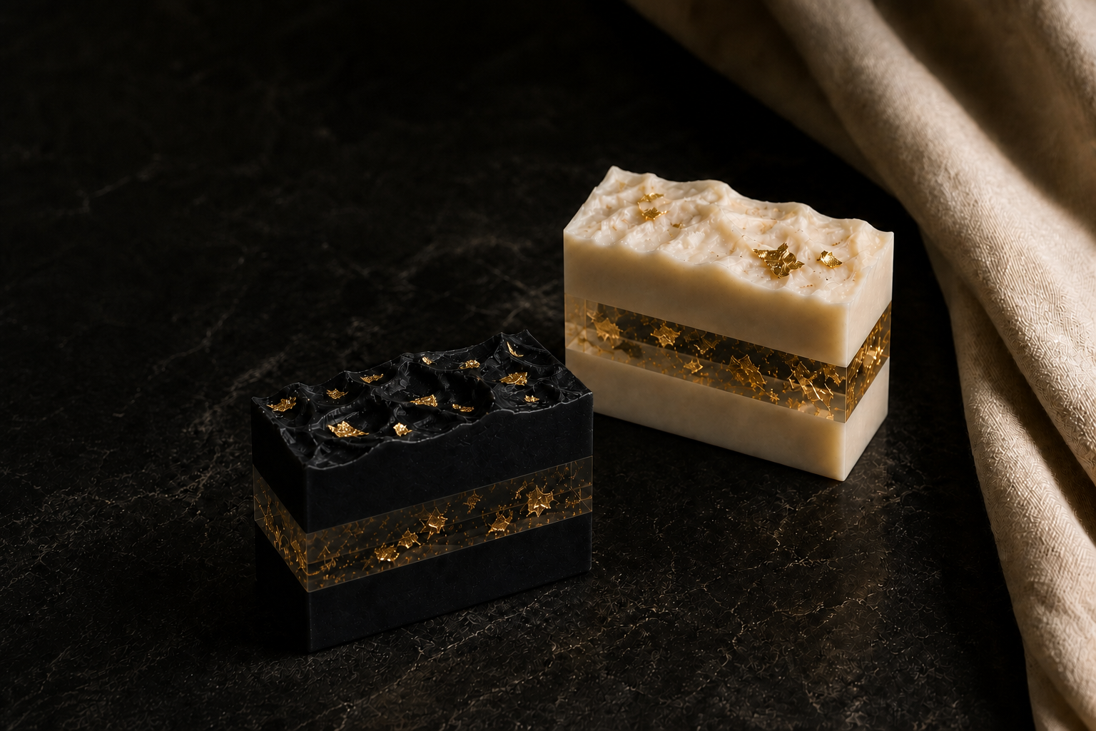 Obsidian and Ivory Reserve soaps topped with gold leaf on dark stone beside ivory linen